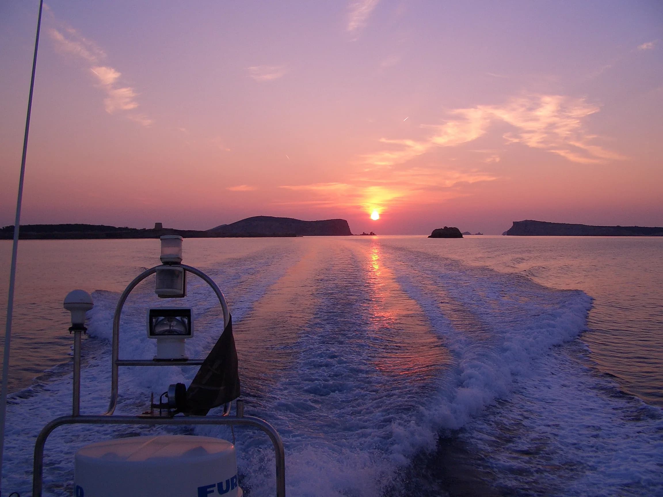 The wake of a boat heading back past the islands as the sun sets over the sea off Ibiza